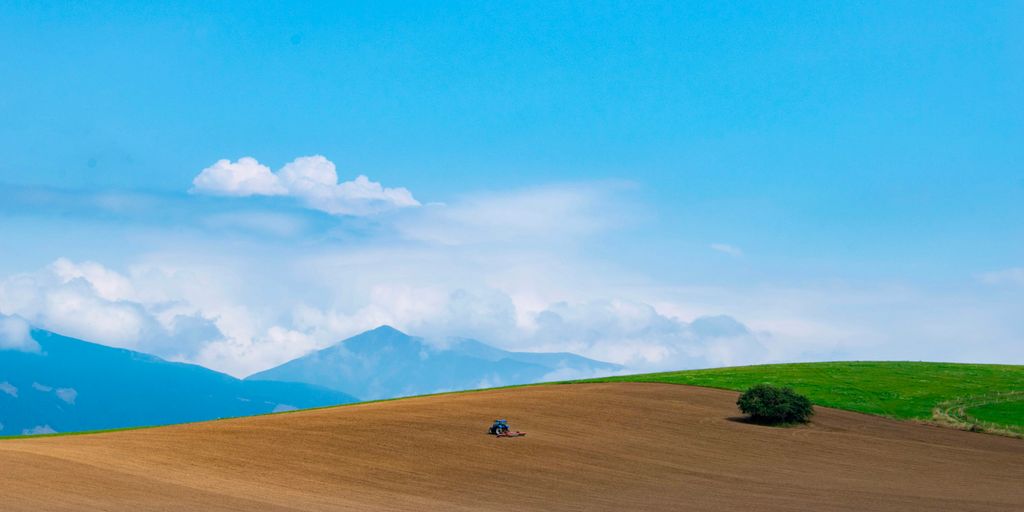 green grass field near mountain under blue sky during daytime